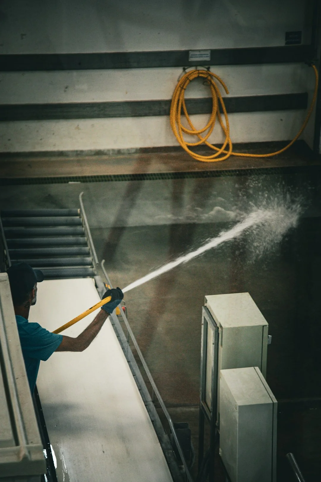 A woman wearing a plaid shirt cleans a kitchen counter using a spray bottle and cloth.